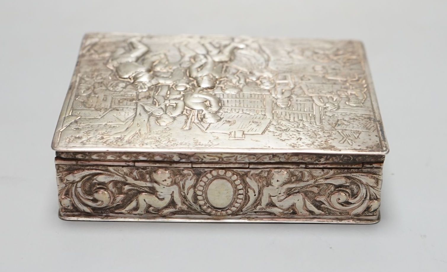 A late 19th / early 20th century German Hanau silver rectangular box and cover, the top embossed with a scene of revellers, import marks for London, 1912, 11.7cm.